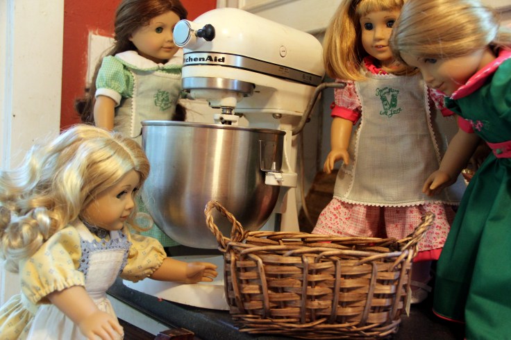 The dolls bake a cake on the "Stitching with Ellie" blog
