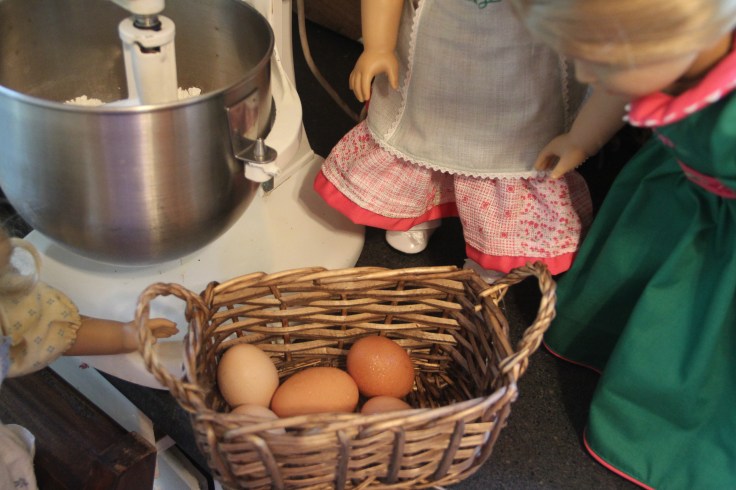 The dolls bake a cake on the "Stitching with Ellie" blog