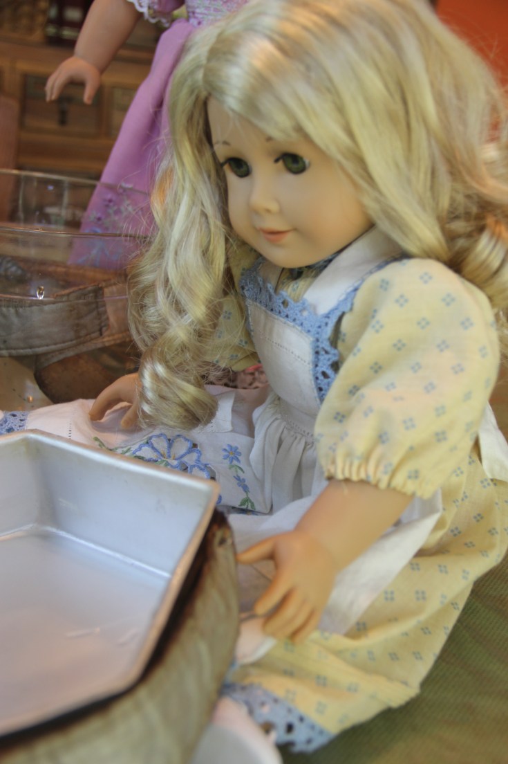 The dolls bake a cake on the "Stitching with Ellie" blog